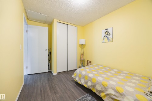 This room features light yellow walls, dark wood-style flooring, and a closet with sliding white doors - Sherwood Park, AB - Indoor Photo Showing Bedroom