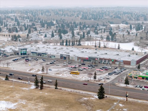 Aerial view showcasing a commercial center with extensive parking, a main road, and surrounding residential areas with mature trees and a body of water - Sherwood Park, AB - Outdoor With View