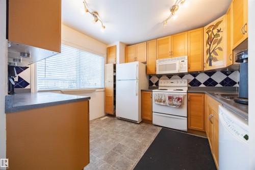 The kitchen features light wood cabinetry, a white refrigerator, a white oven, a white microwave, and a window with blinds - Sherwood Park, AB - Indoor Photo Showing Kitchen
