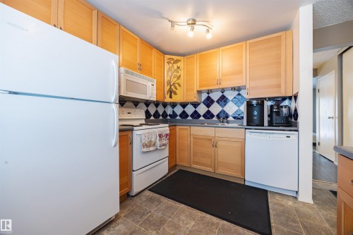 The kitchen features light wood cabinetry, white appliances, and a unique blue and white diamond pattern backsplash - Sherwood Park, AB - Indoor Photo Showing Kitchen