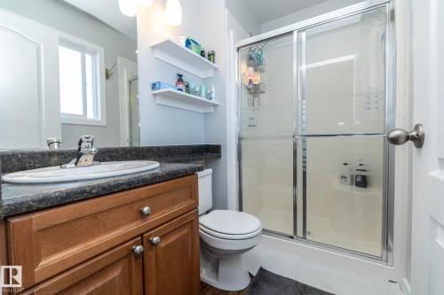 Bathroom featuring a glass-enclosed shower, a wood-finish vanity with a dark countertop, a white oval sink, and a window providing natural light - 65 Birchmont Drive, Leduc, AB - Indoor Photo Showing Bathroom