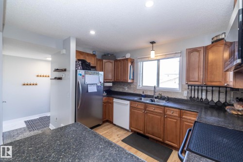 Kitchen featuring wood-finish cabinetry, dark countertop surfaces, double basin sink, and a built-in dishwasher - 65 Birchmont Drive, Leduc, AB - Indoor Photo Showing Kitchen With Double Sink