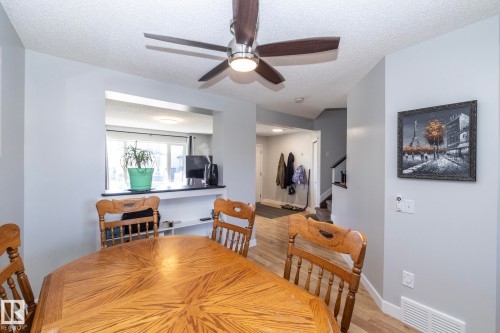 Dining area featuring a wood-finish table, a ceiling fan with integrated lighting, and a pass-through window with a dark countertop - 65 Birchmont Drive, Leduc, AB - Indoor Photo Showing Dining Room