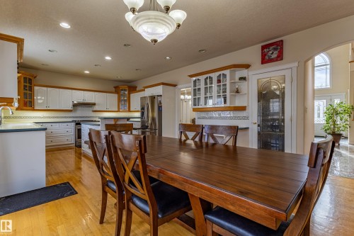 Hardwood flooring throughout the dining area and kitchen, featuring white cabinetry with wood trim, a central kitchen island, and recessed lighting - 195 Kulawy Drive, Edmonton, AB - Indoor Photo Showing Dining Room