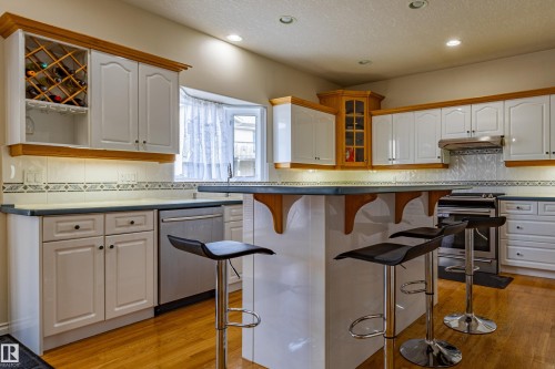 Kitchen featuring white cabinetry with wood trim, a built-in wine rack, and a central island with countertop seating - 195 Kulawy Drive, Edmonton, AB - Indoor Photo Showing Kitchen