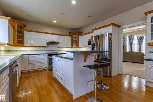 Kitchen featuring wood-finish flooring, white cabinetry with wood trim accents, a central island with an extended breakfast bar, and stainless steel appliances - 195 Kulawy Drive, Edmonton, AB - Indoor Photo Showing Kitchen