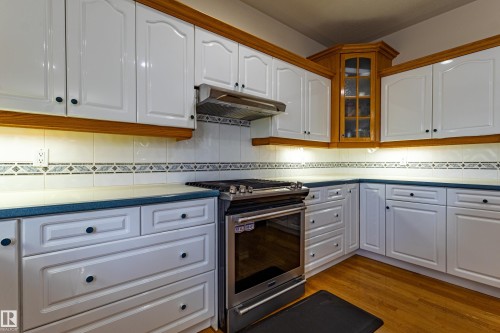 Kitchen featuring white cabinetry with wood trim, a stainless steel range with overhead ventilation, and a corner cabinet with a glass front - 195 Kulawy Drive, Edmonton, AB - Indoor Photo Showing Kitchen