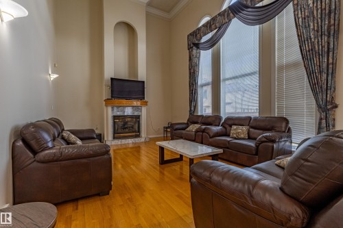 Living area featuring high ceilings, wood-finish flooring, a fireplace with a stone surround, and tall windows with custom drapery - 195 Kulawy Drive, Edmonton, AB - Indoor Photo Showing Living Room With Fireplace