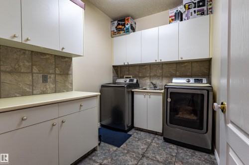 Dedicated laundry space featuring white cabinetry, a tiled backsplash, and durable tile flooring - 195 Kulawy Drive, Edmonton, AB - Indoor Photo Showing Laundry Room