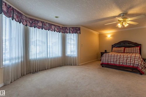 Spacious room featuring a curved bay window with blinds and valance, crown molding, a ceiling fan with light fixture, and wall sconces - 195 Kulawy Drive, Edmonton, AB - Indoor Photo Showing Bedroom