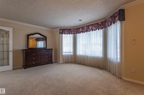 Spacious room featuring a curved bay window with vertical blinds, neutral carpeting, crown molding, and a decorative glass door - 195 Kulawy Drive, Edmonton, AB - Indoor