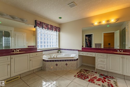Bathroom featuring a corner soaking tub, a large glass block window, double vanity sinks with countertop space, and tile flooring - 195 Kulawy Drive, Edmonton, AB - Indoor Photo Showing Bathroom