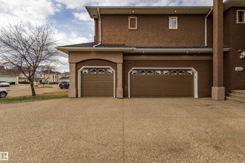 Exterior featuring textured brown stucco, two brown panel garage doors with upper window inserts, a black shingle roof, and a textured aggregate driveway - 195 Kulawy Drive, Edmonton, AB - Outdoor