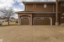 Exterior featuring textured brown stucco, two brown panel garage doors with upper window inserts, a black shingle roof, and a textured aggregate driveway - 195 Kulawy Drive, Edmonton, AB  - Outdoor 