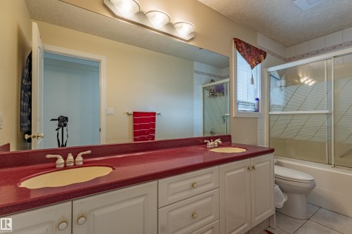Double vanity featuring a red-hued countertop and dual sinks, white cabinetry with gold-toned hardware, full-width mirror, and a shower-tub combination with sliding glass doors - 195 Kulawy Drive, Edmonton, AB - Indoor Photo Showing Bathroom