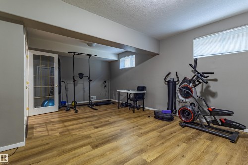 Spacious room featuring wood-finish flooring, two high-set windows with blinds, and neutral painted walls - 195 Kulawy Drive, Edmonton, AB - Indoor Photo Showing Gym Room