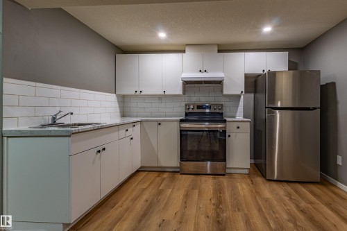 Modern kitchen featuring white cabinetry, subway tile backsplash, light-toned countertops, stainless steel appliances, and wood-finish flooring - 195 Kulawy Drive, Edmonton, AB - Indoor Photo Showing Kitchen