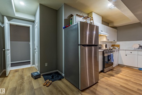 Kitchen area featuring wood-finish flooring, white cabinetry, a stainless steel refrigerator, and a stainless steel range with overhead ventilation - 195 Kulawy Drive, Edmonton, AB - Indoor Photo Showing Kitchen