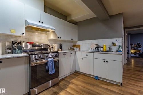 Kitchen featuring white upper and lower cabinetry, subway tile backsplash, stainless steel range with overhead ventilation, light-toned countertops, and wood-finish flooring - 195 Kulawy Drive, Edmonton, AB - Indoor Photo Showing Kitchen