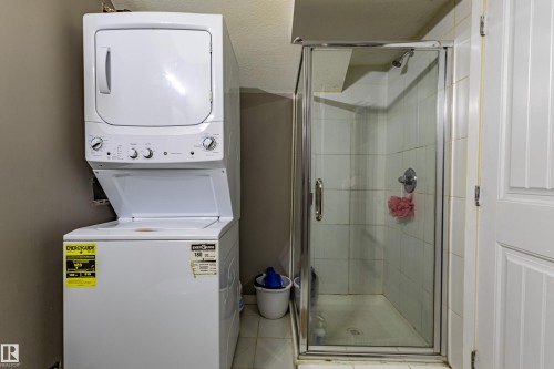 Compact laundry area featuring a stacked washer and dryer, tile flooring, and a glass-enclosed shower with tiled walls - 195 Kulawy Drive, Edmonton, AB - Indoor Photo Showing Laundry Room