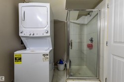 Compact laundry area featuring a stacked washer and dryer, tile flooring, and a glass-enclosed shower with tiled walls - 