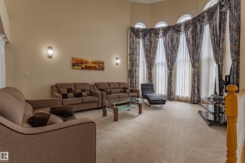 Living area featuring a high vaulted ceiling, large arched windows, sconce lighting, and soft carpet flooring - 195 Kulawy Drive, Edmonton, AB - Indoor