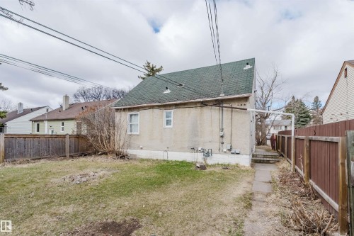 Rear exterior featuring a stucco facade, multiple utility meters, two windows, and a green shingle roof - 12223 127 Street, Edmonton, AB - Outdoor