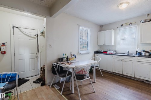 Kitchen area featuring white cabinetry, dark countertops, a stainless steel sink, and wood-finish flooring - 12223 127 Street, Edmonton, AB - Indoor