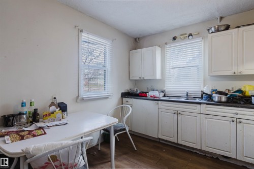 Kitchen featuring white cabinetry, dark countertops, a single basin sink, and two windows with blinds - 12223 127 Street, Edmonton, AB - Indoor Photo Showing Other Room