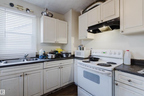 Kitchen featuring white cabinetry, dark countertops, a double basin stainless steel sink, and a white electric range with overhead hood - 12223 127 Street, Edmonton, AB - Indoor Photo Showing Kitchen With Double Sink