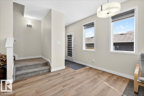 Entry foyer featuring wood-finish flooring, two large windows with roller shades, and a contemporary ceiling fixture - 5315 22 Avenue, Edmonton, AB - Indoor Photo Showing Other Room