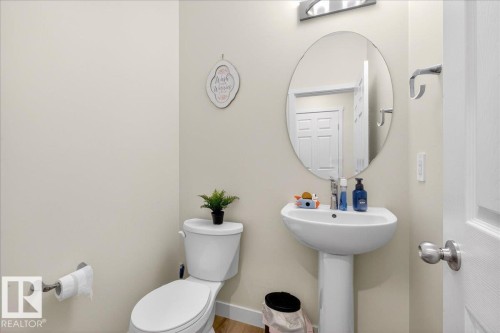 Pedestal sink with an oval mirror, modern wall-mounted light fixture, and wood-finish flooring - 5315 22 Avenue, Edmonton, AB - Indoor Photo Showing Bathroom
