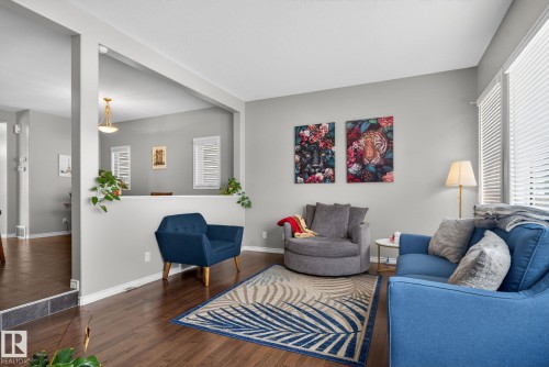 Open-concept living space with dark wood-finish flooring, light grey walls, white baseboards, and ample natural light from large windows with horizontal blinds - 6912 22 Avenue, Edmonton, AB - Indoor Photo Showing Living Room