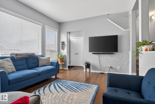 Bright living area featuring wood-finish flooring, light grey walls, and prominent windows with horizontal blinds - 6912 22 Avenue, Edmonton, AB - Indoor Photo Showing Living Room