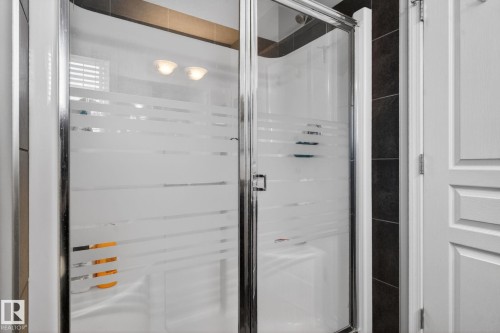 Glass shower enclosure with frosted privacy bands, chrome frame, and dark tile surround - 6912 22 Avenue, Edmonton, AB - Indoor Photo Showing Bathroom
