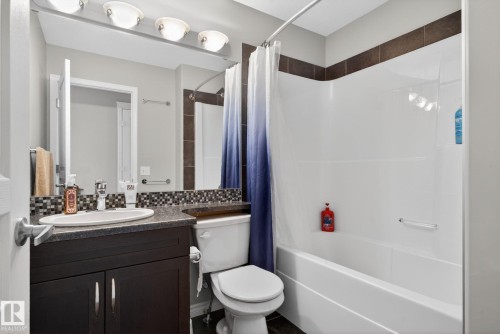 Bathroom featuring a dark wood-finish vanity with a built-in sink, stone-look countertop, mosaic tile backsplash, and a large wall mirror - 6912 22 Avenue, Edmonton, AB - Indoor Photo Showing Bathroom