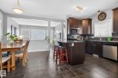 Open-concept kitchen featuring dark wood cabinetry, stainless steel appliances, dark tile flooring, a breakfast bar, and a tile backsplash - 6912 22 Avenue, Edmonton, AB  - Indoor 