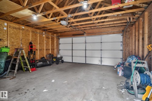 Single-car garage featuring a sectional overhead door, exposed wood framing, OSB wall sheathing, concrete flooring, and overhead lighting - 6912 22 Avenue, Edmonton, AB - Indoor Photo Showing Garage