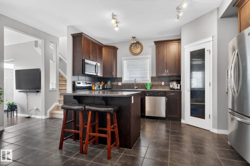 Kitchen featuring dark wood-finish cabinetry, stainless steel appliances, a center island with seating, and dark tile flooring - 6912 22 Avenue, Edmonton, AB - Indoor Photo Showing Kitchen