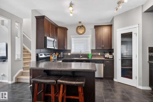 Kitchen featuring dark wood cabinetry, dark stone-finish countertops, stainless steel appliances, and a mosaic tile backsplash - 6912 22 Avenue, Edmonton, AB - Indoor Photo Showing Kitchen With Double Sink