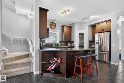 Modern kitchen featuring dark wood cabinetry, stainless steel appliances, a breakfast bar with built-in shelving, dark countertops, and a complementary tile backsplash - 6912 22 Avenue, Edmonton, AB - Indoor Photo Showing Kitchen