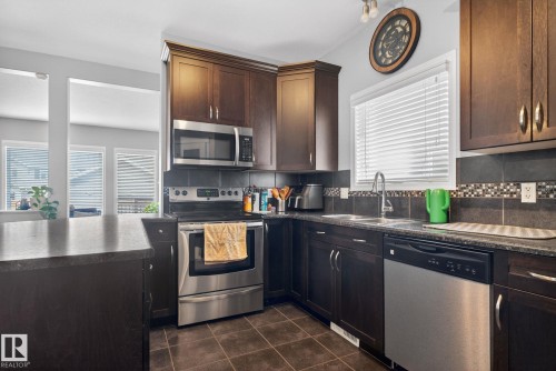 Kitchen featuring dark wood cabinetry, stainless steel appliances, and dark tile flooring - 6912 22 Avenue, Edmonton, AB - Indoor Photo Showing Kitchen