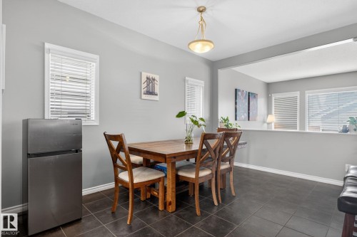 Dining area featuring dark floor tiles, light gray walls, a built-in architectural opening, white window frames with blinds, and an overhead dome light fixture - 6912 22 Avenue, Edmonton, AB - Indoor Photo Showing Dining Room
