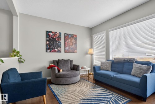 Spacious living area featuring expansive windows with white blinds, wood-finish flooring, and light gray walls - 6912 22 Avenue, Edmonton, AB - Indoor Photo Showing Living Room