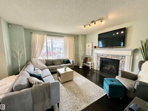 Hardwood-finish flooring complements a decorative fireplace with a patterned tile surround and white mantel - 17936 85 Street, Edmonton, AB - Indoor Photo Showing Living Room With Fireplace