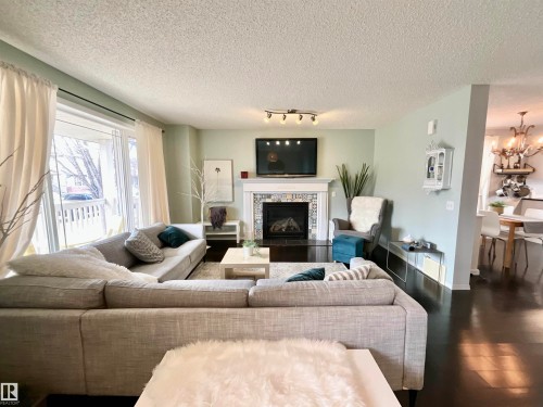 Living room featuring a fireplace with decorative tile surround and white mantel, dark wood-finish flooring, a large window with white trim, and light-colored walls - 17936 85 Street, Edmonton, AB - Indoor Photo Showing Living Room With Fireplace