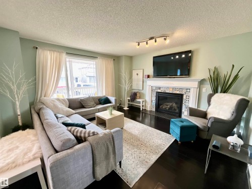 Living area featuring dark wood-finish flooring, a decorative fireplace with patterned tile surround, and a large window with white curtains - 17936 85 Street, Edmonton, AB - Indoor Photo Showing Living Room With Fireplace