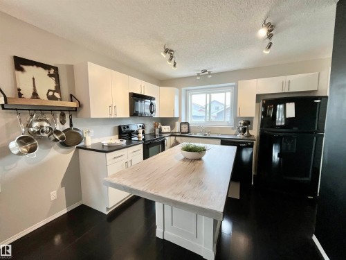 Kitchen featuring dark wood-finish flooring, white cabinetry with silver hardware, black countertops, and a central island with a light wood-finish top - 17936 85 Street, Edmonton, AB - Indoor Photo Showing Kitchen