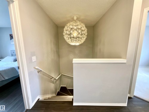 Elegant modern chandelier illuminates the stairwell with dark wood-finish flooring, white trim, and a white handrail - 17936 85 Street, Edmonton, AB - Indoor Photo Showing Other Room