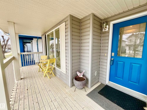 Covered front porch featuring wood-finish decking, white railings, and a bright blue entry door with a glass insert - 17936 85 Street, Edmonton, AB - Outdoor With Deck Patio Veranda